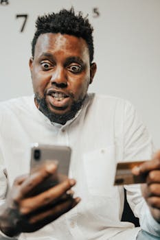 A surprised man holding a credit card and smartphone, engaged in online shopping.