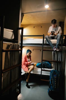 Young travelers enjoy downtime in a hostel bunk room, using technology for planning.